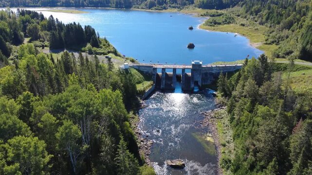 Panoramic aerial view looking down towards the old Mitis Dam until it makes a passage inside its water evacuation and level control structure of Lake Mitis. Quebec, Canada, 2025.