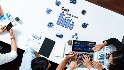 Dynamic scene of a team collaborating to strategize cost reduction with data analysis tools, featuring graphs and digital insights in a modern office environment. Raster