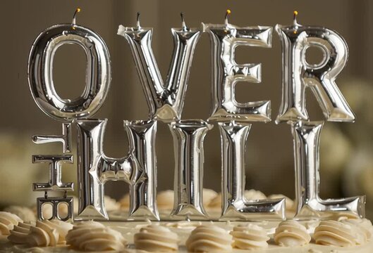Birthday Cake with Candles that spell "Over The Hill" - funny 40th b-day concept, candle letters create humorous message for forty year old bday. Zoom in, flame blows out.