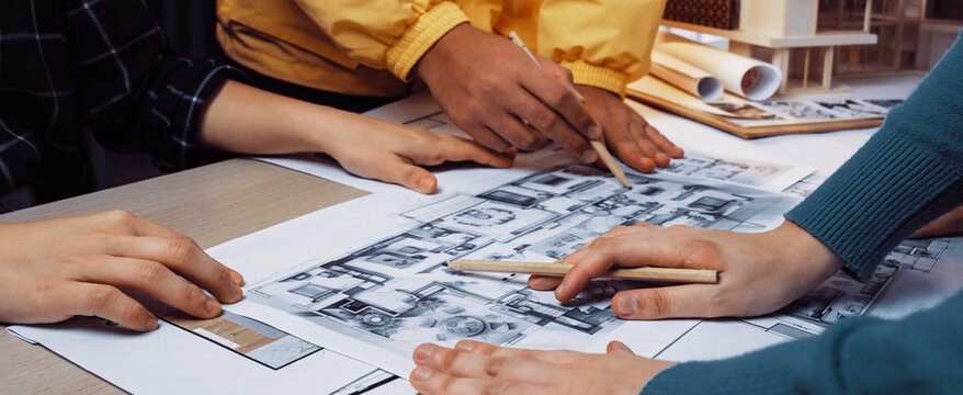 A diverse group of individuals collaborates over detailed blueprints in a modern workspace, demonstrating teamwork and creativity in the architectural planning process. SACTR - Powered by Adobe