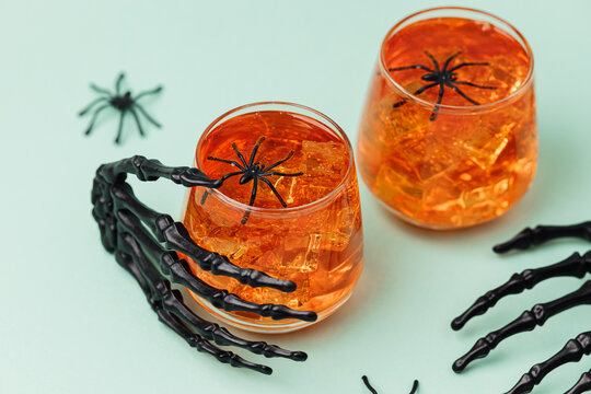 Spooky Halloween orange drinks with ice and plastic spiders held by skeleton hands
