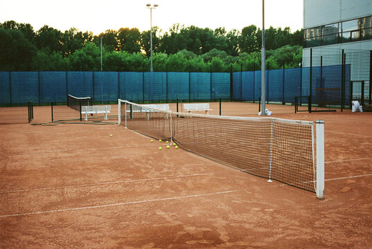 Tennis court at sunset with scattered balls and empty benches