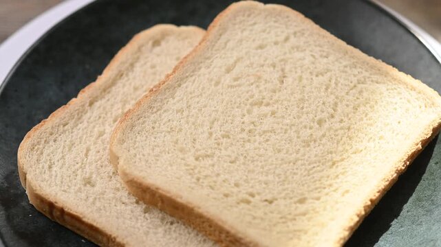 Two slices of white bread rotating on a black plate