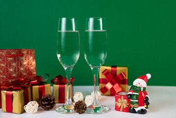 Two champagne glasses with stacked gift boxes and festive accents on green, classic holiday party image for seasonal marketing. 