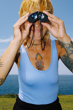 Person using binoculars on a sunny day by the ocean