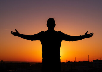 Fototapeta premium Silhouette of a person with open arms embracing the vibrant sunset sky, symbolizing freedom and hope.