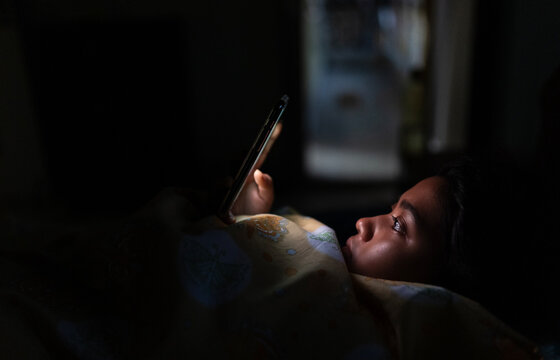 Young Indian woman lying on bed and browsing smartphone at nighttime