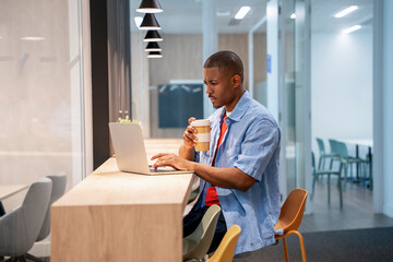 Focused businessman working on laptop and drinking coffee in office