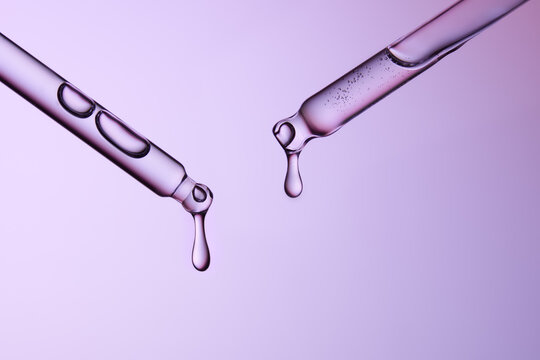 Two glass pipettes with liquid on gradient blue and purple backdrop.