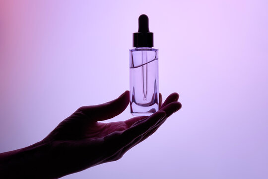 Hand Holding a Transparent Dropper Bottle on Gradient Background