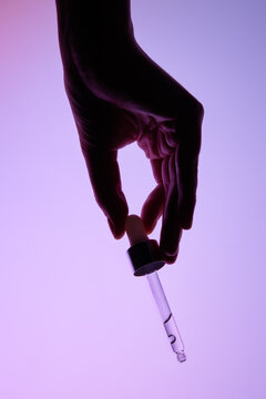 Hand Holding a glass pipette with moisturizer on a Gradient Background