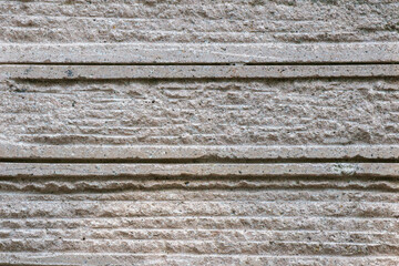 Close-up of textured concrete wall with horizontal carved lines and rough surface detail in neutral gray tones