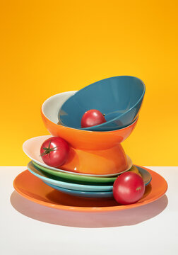 Various Bright Bowls and red Tomatoes on orange Background. 