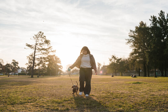 Woman walking with her dachshund in a park at sunset