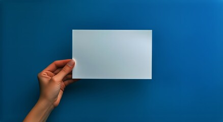Hand Holding Blank Paper Over a Vibrant Blue Surface in a Creative Workspace