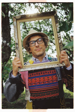 Creative individual poses with a frame against apple garden trees