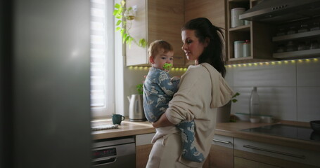 Obraz premium Mother holding baby near kitchen counter, smiling and bonding with child, warm and nurturing parenting moment during everyday family routine