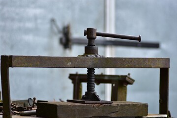 Vintage rusty metal press tool with handle and screw, industrial heritage object symbolizing mechanical work, workshop atmosphere and retro engineering history.