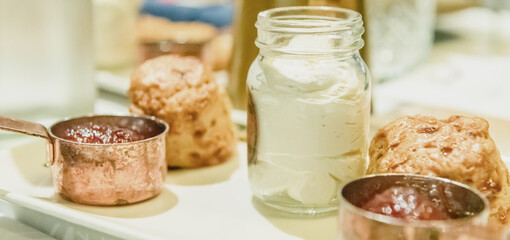 Classic British Scones with Jam and Cream. A plate of warm, golden scones with clotted cream and strawberry jam in rustic copper pots. This authentic and delicious image captures the essence