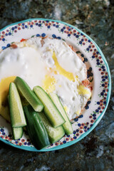 Delicious breakfast dish with fried eggs and fresh cucumber slices on a decorative plate