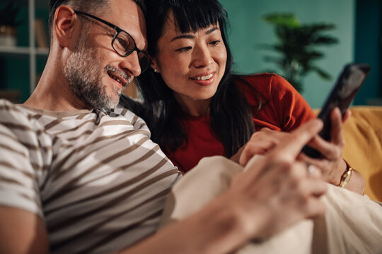 Happy couple relaxing on sofa browsing smartphone together at home