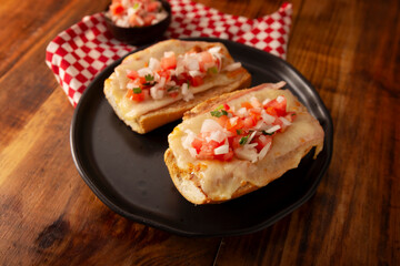 Molletes. Mexican recipe based on bolillo bread split lengthwise, spread with refried beans and gratin cheese, adding pico de gallo sauce and some protein such as ham, bacon or chorizo.