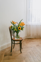 Bouquet of autumn flowers with lilies, gladiolus and sunflowers in a glass vase, placed on a wooden vintage chair. Warm rustic still life.	