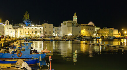 Night view of Trani harbor in Apulia, Italy, with boats and reflections