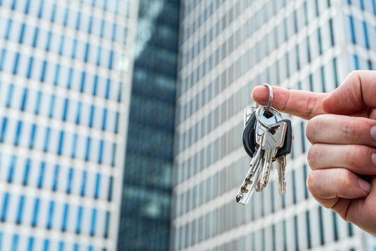 Keys to the Future: Unlocking Opportunities in the Modern City. Symbolic image of a hand holding keys with a blurred futuristic glass building in the background