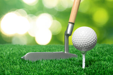 Golf ball, tee, club and green grass against blurred background