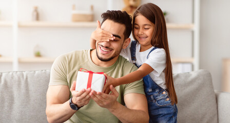 Portrait of cute little girl holding and giving wrapped gift box, making surprise for her excited...