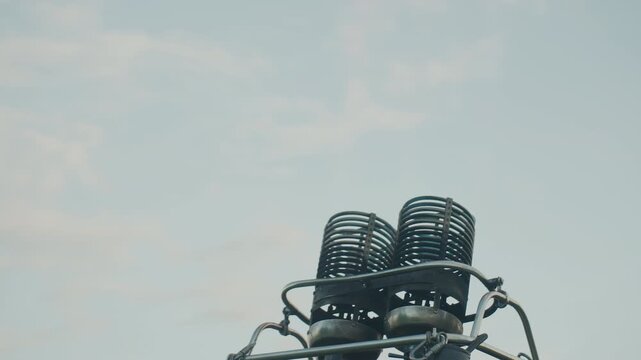 close up of metal burner coils igniting twin orange flames above wicker basket of hot air balloon causing fire to flicker through spirals against pale sky at dusk during flight launch preparation