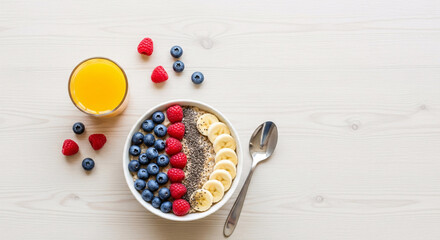 A healthy and colorful breakfast bowl filled with blueberries, raspberries, chia seeds, and sliced bananas, served with a glass of orange juice.