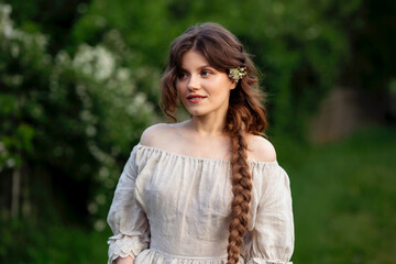 Fototapeta premium Beautiful woman with long braid in vintage dress posing in jasmine flowers in countryside 