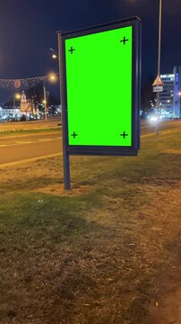 Vertical handheld footage of a city street at night, showing moving cars and brightly lit buildings, with a green screen billboard perfect for adding custom digital ads or promotional content, 4k.