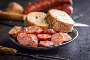 Smoked sliced sausages and bread on plate on black table.