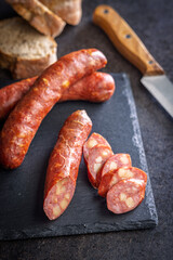 Smoked sliced sausages on cutting board on black table.