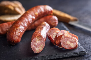 Smoked sliced sausages on cutting board on black table.