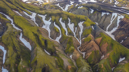 Drone aerial of volcanic mountains in Iceland with erosion lines snow fields and vibrant moss textures