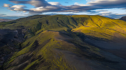 Aerial view of Icelandic volcanic mountain slopes with green moss patches under dramatic evening clouds in remote highland wilderness