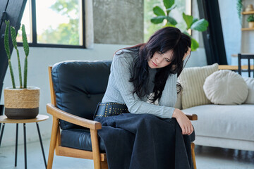 Unhappy upset young woman having headache, sitting on chair at home