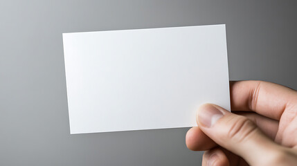 Obraz premium Blank white card in hand against gray background. Simple and clean design concept for stationery, promotion, or contact information display. Minimalist.