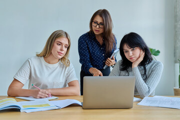 Two university student girls with female teacher mentor study while sitting at desk