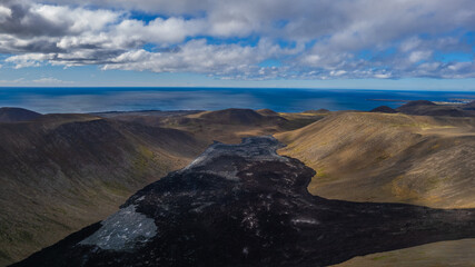 Dark lava flow in Icelandic highlands surrounded by rolling hills and mountains with the North...