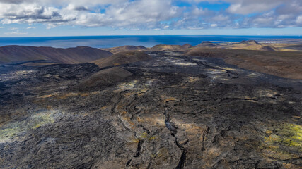 Aerial view of vast black lava field in Iceland with cracks and rugged rock textures stretching toward the distant ocean horizon