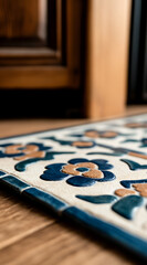 Naklejka premium Close-up of a decorative tile mat with floral designs in blue and tan, positioned on a wooden floor near a partially visible wooden door.