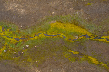 Aerial view of bright green moss and small stream cutting across dark volcanic ground in Icelandic highlands showing raw untouched nature