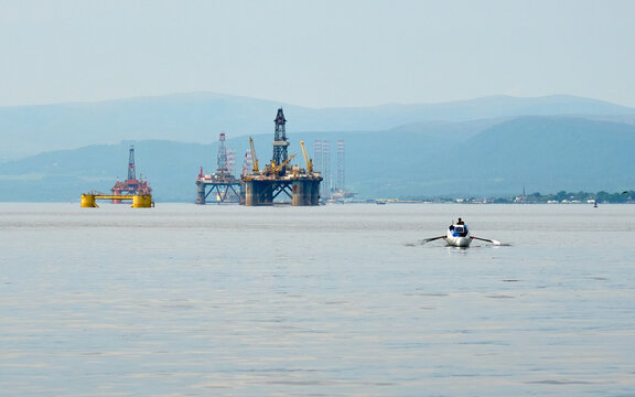 Energy transition - boat with solar panel rowing past former oil rigs