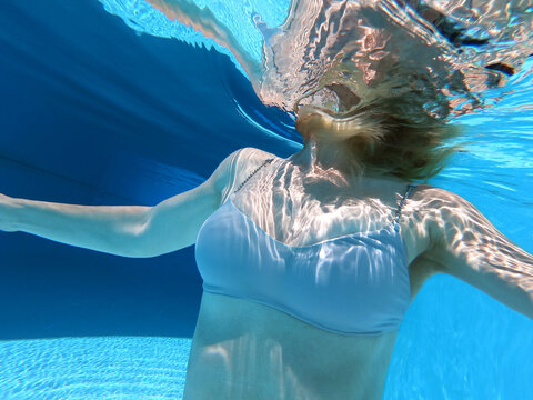 Woman in grey bikini underwater in a turquoise swimming pool