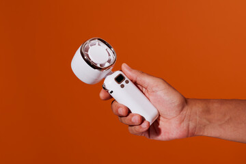 a man grips a white handheld fan with chrome rim on an orange setting